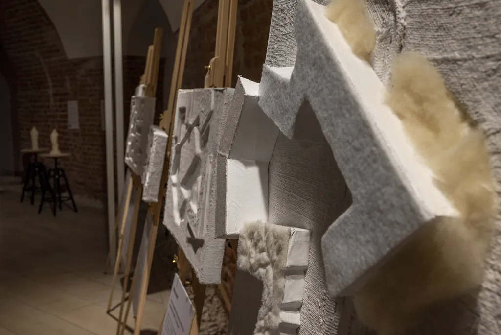 Lucrări tactile cu forme arhitecturale 3D expuse pe șevalete într-o galerie de cărămidă.