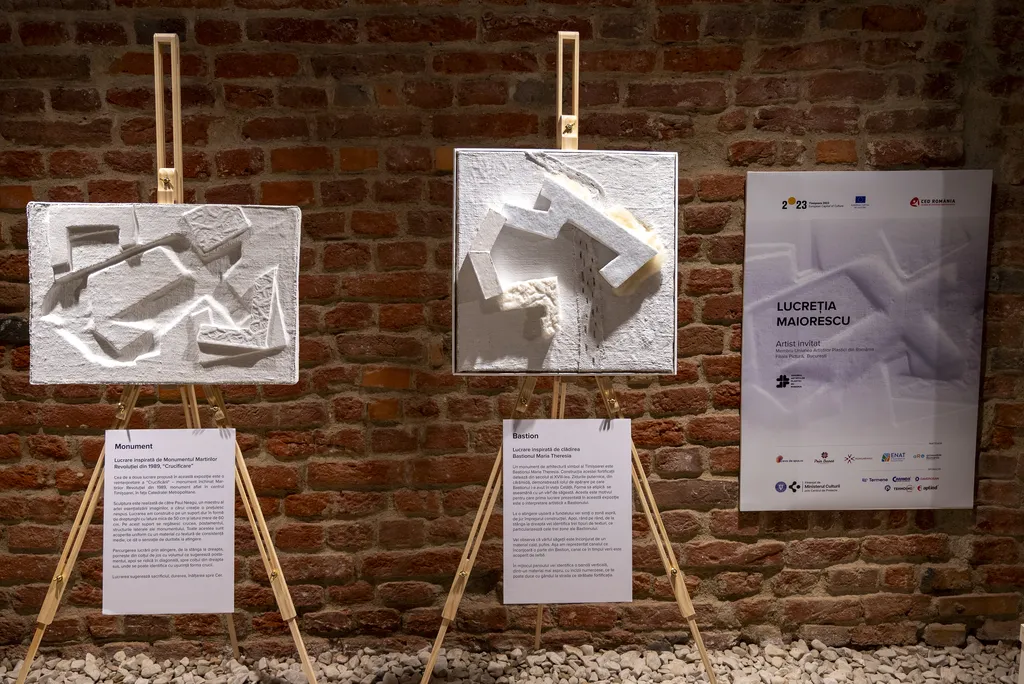 Lucrări tactile cu forme arhitecturale 3D expuse pe șevalete într-o galerie de cărămidă.